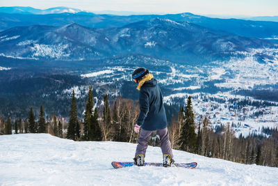 Rear view of man with snowboard standing on snow covered land