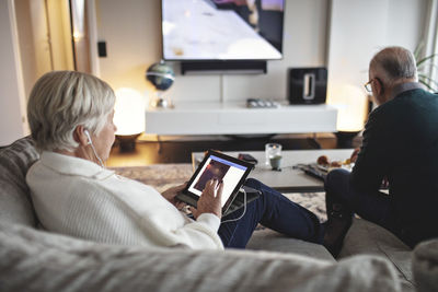 Senior woman using digital tablet while male partner sitting on sofa in living room