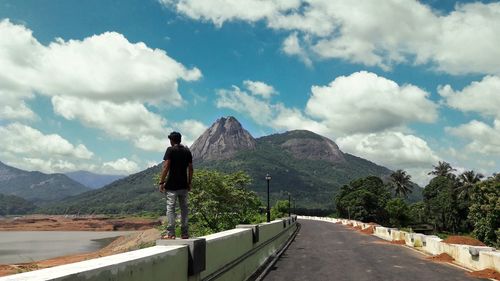 Rear view of man standing on mountain against sky