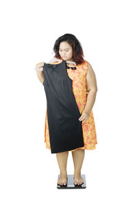 Full length of woman holding dress while standing on weight scale against white background