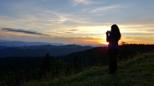 Full length of woman photographing on mountain against sky during sunset