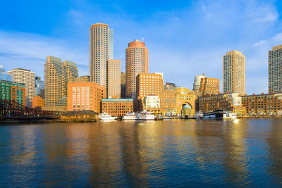 Illuminated buildings by river against sky in city