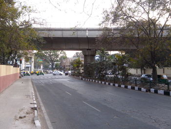 Road by trees in city against sky