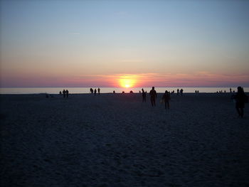 Silhouette people on beach against sky during sunset