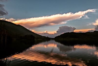 Scenic view of lake by silhouette mountains against sky during sunset