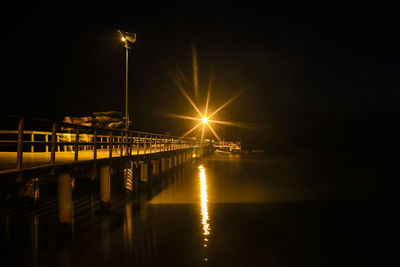 Illuminated pier over river against sky at night