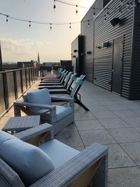 Empty chairs on footpath by buildings against sky