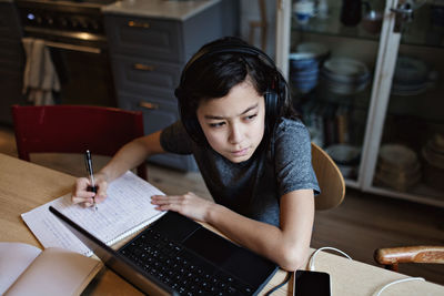 High angle view of thoughtful boy looking away while writing on book at home