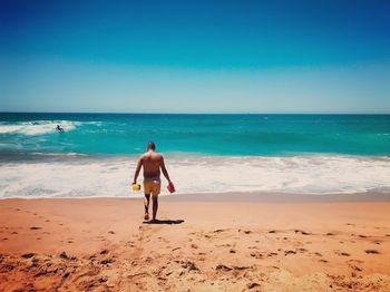 Rear view of shirtless man on beach against sky