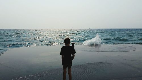 Rear view of boy standing on pier against clear sky