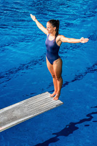 Mid adult woman with arms outstretched standing on diving platform