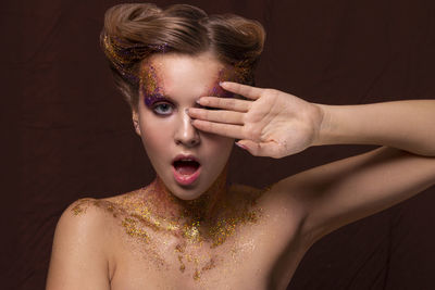 Portrait of young woman with glitter against black background