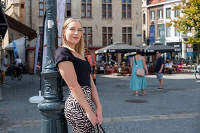 Portrait of young woman standing on street in city