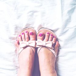 Low section of woman wearing sandals on bed