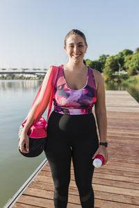 Smiling sportswoman with bag standing on pier