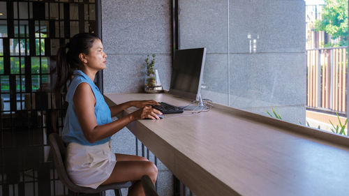 Side view of young woman using mobile phone while sitting at home