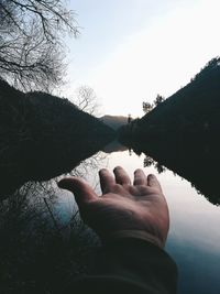 Cropped hand of person showing lake amidst trees against sky