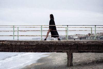 Side view of young woman walking on pier against sky