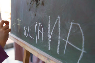 Cropped image of hand writing on blackboard