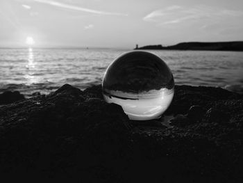 Close-up of crystal ball on rock at beach against sky