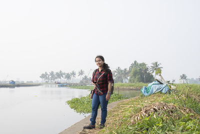 Portrait of young woman standing by river against sky