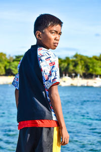 Young man looking away while standing by sea against sky