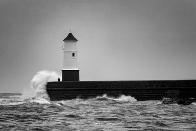 Lighthouse by sea against clear sky