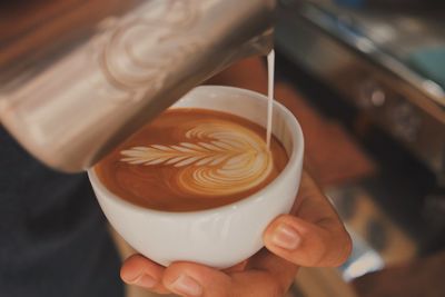 Cropped hand pouring milk in cup