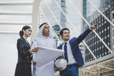 Business people looking at businessman pointing against metallic structure