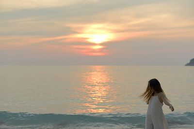 Rear view of woman standing at beach during sunset