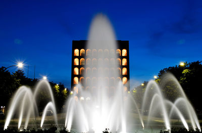 Illuminated fountain in city against sky at night