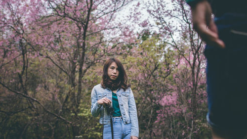 Woman holding camera while standing against tree