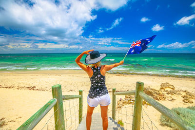Rear view of woman holding australian flag on steps at beach
