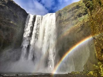 Low angle view of waterfall against cloudy sky