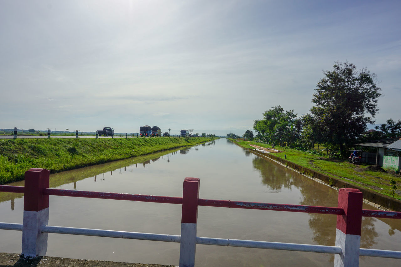 water, sky, nature, plant, landscape, cloud, waterway, river, environment, railing, architecture, beauty in nature, scenics - nature, tranquility, tree, land, body of water, reflection, no people, outdoors, shore, fence, walkway, built structure, day, tranquil scene, rural scene, morning, travel destinations, travel, tourism, sunlight, grass, non-urban scene, vacation