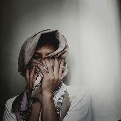 Portrait of man covering face with scarf against wall