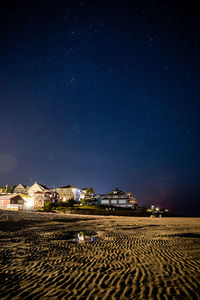 Stars in the night sky above beach houses at low tide.