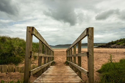 Boardwalk leading towards footbridge against sky