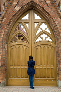 A woman is facing the huge gate of a catholic church, trying to open the door.