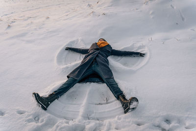 A young woman makes a snow angel lying in the snow with her arms and legs spread to the sides