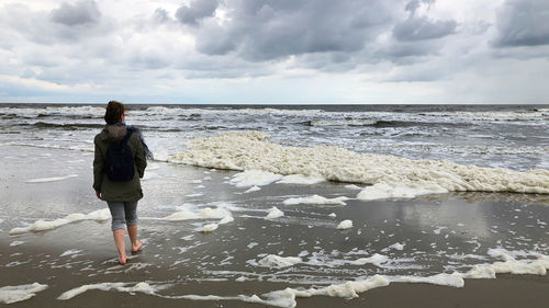 Rear view of woman standing on beach against sky