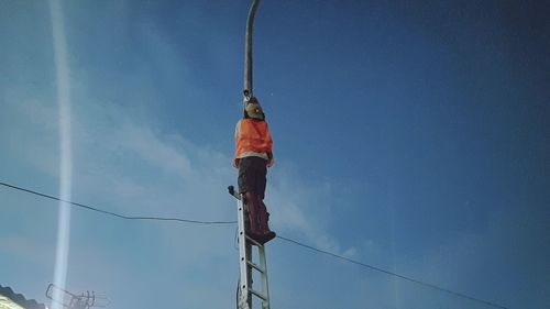 Low angle view of man working on rope against sky