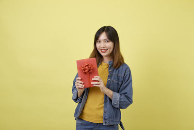 Portrait of smiling young woman against yellow background