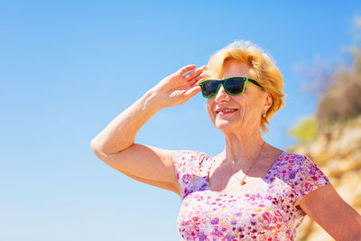 Elderly woman in sunglasses looking at the sea and having fan.