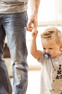 Midsection of father holding baby boy's finger at home