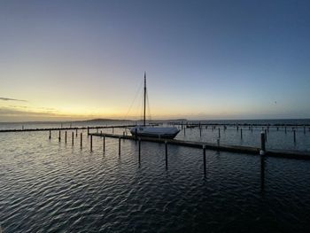 Sailboats moored in sea against clear sky during sunset