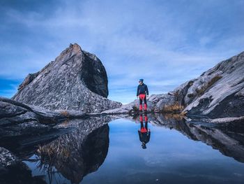 Man standing at pond on mountain against sky