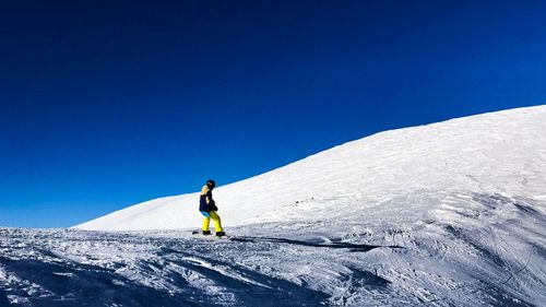 Man skiing on snowcapped mountain against clear blue sky