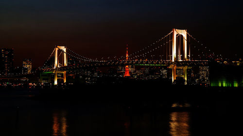 Low angle view of illuminated rainbow bridge over river against sky at night