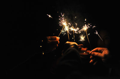 Close-up of people holding sparklers at night